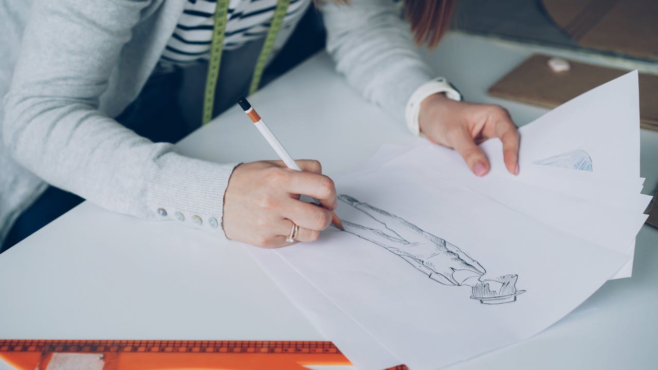 Fashion designer drawing sketches on paper, focusing on creativity and design.